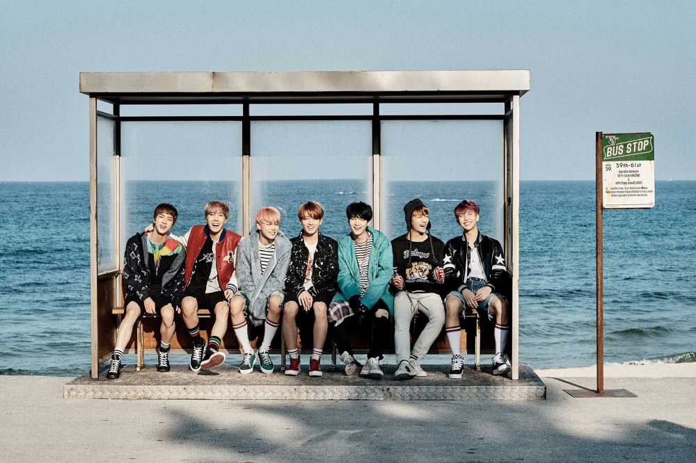 BTS seven men sitting at a bus stop in front of the ocean