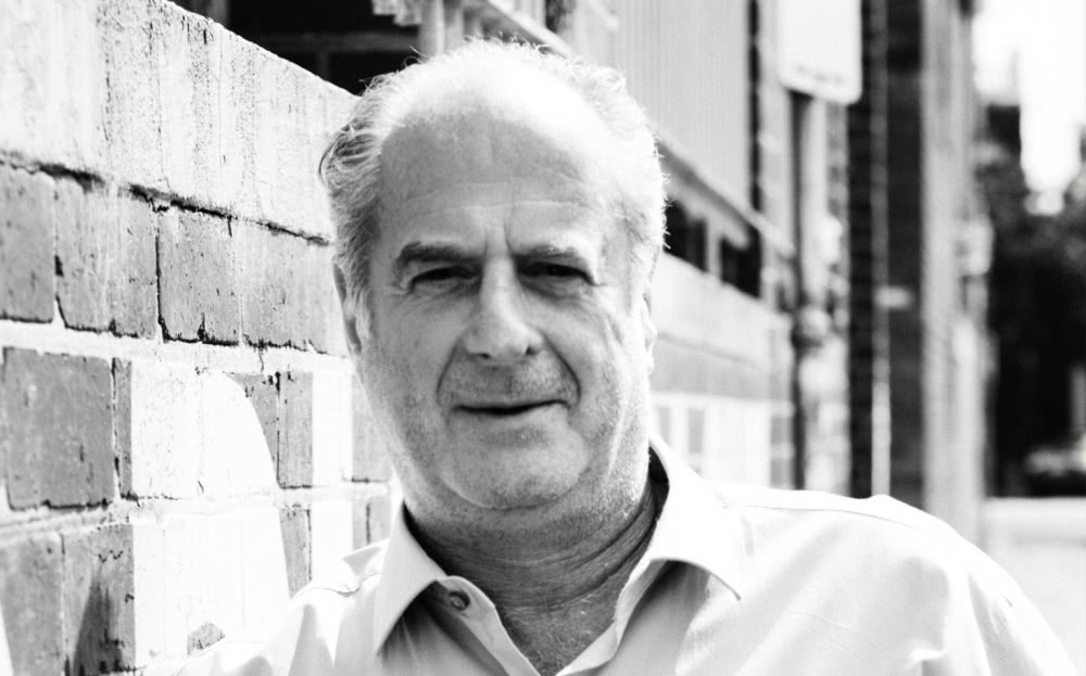 Black & white close up image of Michael Gudinski leaning against a brick wall for good neighbour of power players